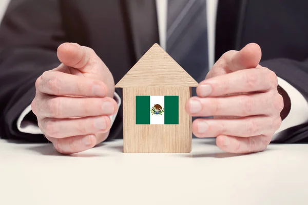 Businessman hand holding wooden home model with Mexican flag. insurance and property concepts