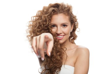 Ayrı bir kadın işaret ediyor. Doğal makyajlı, kıvırcık uzun saçlı ve beyaz arka planda dostça gülümseyen güzel bir kadın modeli.