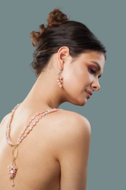 Neşeli, şık, esmer model, makyajlı, dalgalı saç stili ve mavi arka planda poz veren sağlıklı tenli. Kolyeli bir kadının portresi.