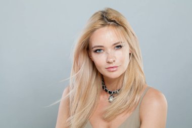 Çekici, genç ve güzel bir bayan model, uzun renkli saçları ve sağlıklı deri portresi var. Sarışın kadın gri stüdyo arka planındaki kameraya bakıyor.