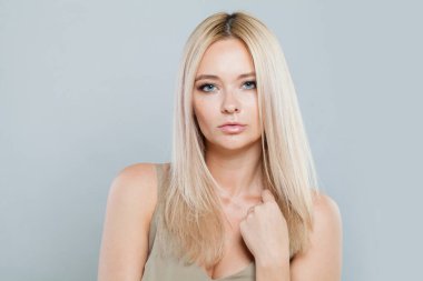 Uzun renkli saçları ve sağlıklı deri portresi olan göz kamaştırıcı genç bir bayan model. Sarışın kadın gri stüdyo arka planındaki kameraya bakıyor.