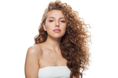 Doğal makyajlı, temiz ciltli ve beyaz arka planda dalgalı saçlı çekici bir genç kadın.