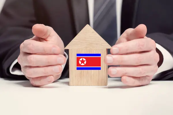 Businessman hand holding wooden home model with North Korean flag. insurance and property concepts