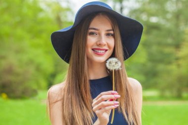 Neşeli esmer kadın portresi. Uzun saçlı ve makyajlı güzel bir kadın model. Baharın bahçesinde klasik mavi şapka takıyor.