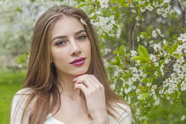 Beautiful young woman with natural makeup and healthy long brown hair in blossom park outdoors. Natural female beauty portrait