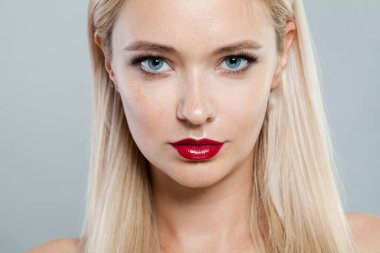 Makyajlı, uzun sarı saçlı, beyaz stüdyo duvarına yaslanmış genç bir kadının yakın plan fotoğrafı.