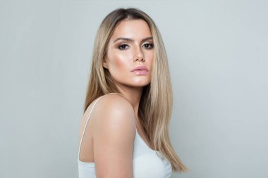 Temiz tenli, uzun ve sağlıklı sarı saçlı, beyaz arka planda gülümseyen güzel bir model kadın. Yüz bakımı, saç bakımı ve kozmetik konsepti