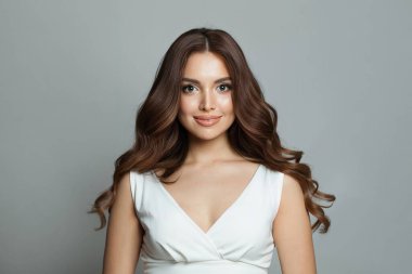 Güzel esmer, temiz tenli, güzel dalgalı saçlı ve doğal makyajlı, gri arka planda poz veren güzel bir kadın. Moda güzeli kadın portresi