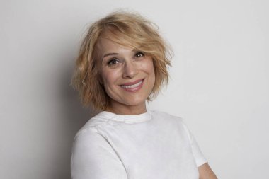 Beyaz duvarda sevimli gülüşü olan neşeli olgun bir kadın.