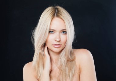 Poz veren kadın yüzü yakın plan. Taze ciltli sarışın manken ve siyah arka planda sağlıklı ipek saçlı. 