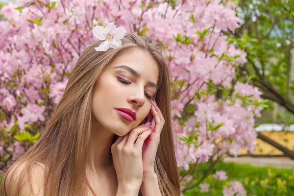 Uzun kahverengi saçlı, çiçekli arka planda doğal makyajlı güzel bir manken.