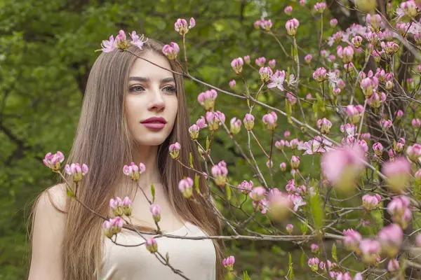 Lovely young woman with natural makeup and healthy long brown hair in blossom park outdoors. Natural female beauty portrait