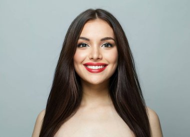 Uzun, sağlıklı saçları ve beyaz arka planda poz veren ipek tenli neşeli, genç bir kadın. Moda stüdyosu portresi