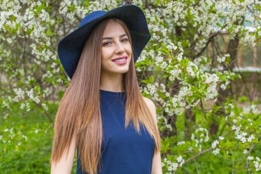 Uzun kahverengi saçlı ve çiçekli arka planda doğal makyajlı bir mankenin açık hava portresi.