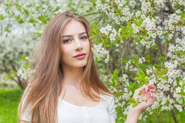 Moda modelinin yakın plan portresi. Uzun kahverengi saçlı ve doğal makyajlı. Çiçekli arka planda.
