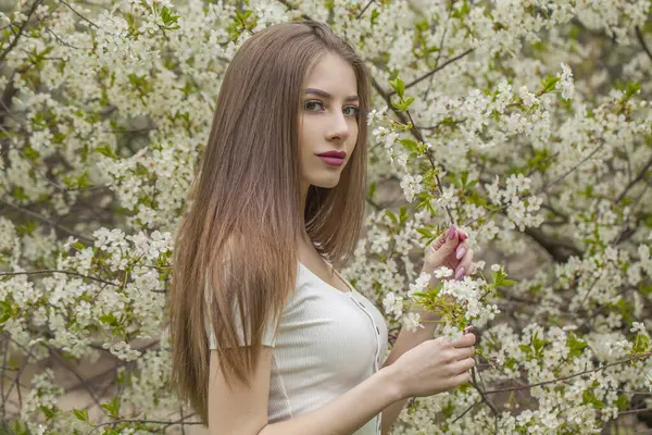Fashionable young woman with natural makeup and healthy long brown hair in blossom park outdoors. Natural female beauty portrait