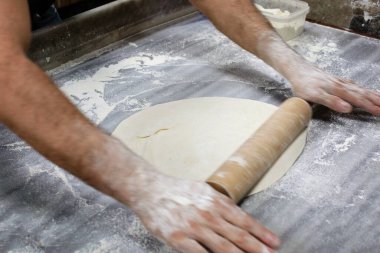 Tahta masa üzerinde merdaneli hareketli elleri olan Hamur.