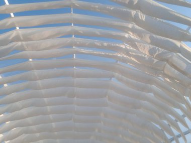 Beyaz tasarım bantları, açık havada esen deniz melteminin üzerindeki kumaştan beyaz perdelerle tente döker.