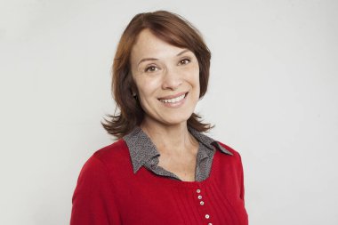 Kahverengi saçlı, tatlı gülümseyen, beyaz arka planda kameraya bakan hoş, olgun bir kadın.