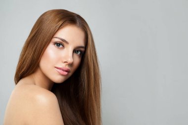 Gri arka planda uzun saçlı ve temiz tenli bir kadının portresi. Doğal kozmetik ve tatlı gülüşlü kadın modelin güzel yüzü