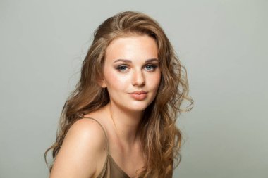 Makyajlı, açık tenli ve beyaz arka planda uzun dalgalı saç modelli güzel bir kadın modeli. Moda stüdyosu genç bir kadının portresi.