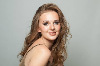Gülümseyen, makyajlı, temiz ciltli ve beyaz arka planda uzun dalgalı saç modeli. Moda stüdyosu genç bir kadının portresi.