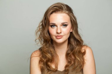 Makyajlı, pürüzsüz ciltli ve beyaz arka planda uzun dalgalı saç modelli göz alıcı bir kadın modeli. Moda stüdyosu genç bir kadının portresi.