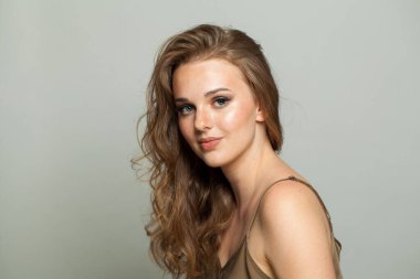 Makyajlı, temiz ciltli ve beyaz arka planda uzun dalgalı saç modelli mutlu bir kadın modeli. Moda stüdyosu genç bir kadının portresi.