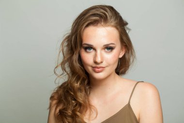 Makyajlı, pürüzsüz ciltli ve beyaz arka planda uzun dalgalı saç modelli mükemmel bir kadın modeli. Moda stüdyosu genç bir kadının portresi.