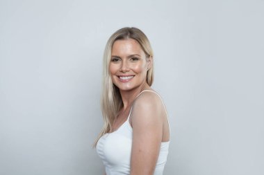 Çekici sarışın kadın, uzun saçlı ve sağlıklı temiz tenli beyaz arka planda duruyor.