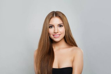 Gri arka planda uzun saçlı ve temiz tenli çekici bir kadın. Doğal kozmetik ve tatlı gülüşlü kadın modelin güzel yüzü