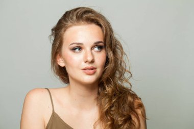 Kadın yana bakıyor. Makyajlı ve uzun dalgalı saçlı genç bayan, yakın plan portresi.