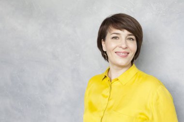 Neşeli olgun kadın gri arka planda kameraya bakıyor, stüdyo portresi.
