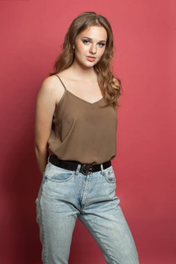 Kırmızı stüdyo arka planında duran açık renk ceketli, ipek elbiseli genç bir kadın.