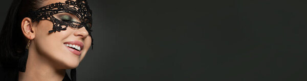 Счастливая возбужденная женщина в карнавальной маске на фоне черного баннера. Маскарад, вечеринка; концепция моды и гламура