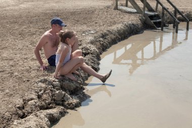 Happy father and daughter resting on mud geyser resort with therapeutic mud outdoors clipart