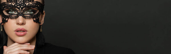 Красивая молодая женщина в карнавальной маске на фоне черного баннера. Маскарад, вечеринка; концепция моды и гламура