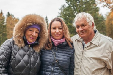 Dışarıda büyükannenle büyükbabana sarılan bir kadın. Mutlu büyükanneler, büyükbabalar ve kızları neşeli mutluluklar, sevgi ve ihtiyarlara bakıyorlar.