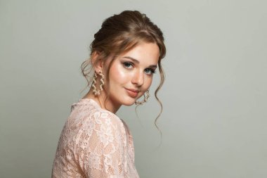 Taze tenli neşeli zarif bir kadın, beyaz arka planda updo saçlı ve makyajlı. Güzel yüz yakın plan