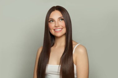 Gülümseyen genç kadın modeli, doğal makyaj ve uzun düz kahverengi saç portresi. Yüz bakımı, kozmetoloji, cilt bakımı ve güzellik salonu konsepti