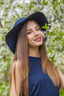 Doğal makyajlı, uzun düz saçlı, bahar çiçeği bahçesinde poz veren zarif genç bir kadın.