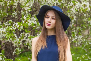 Doğal makyajlı ve uzun düz saçlı çekici bir genç kadın. Baharın çiçek bahçesi parkında poz veriyor.