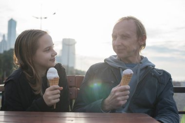 Baba ve küçük kızı kafede dinleniyor, güneşli bir günde dondurma yiyorlar. Mutluluk ve hatıralar.