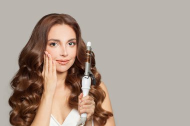 Beyaz arka planda saç maşası kullanan güzel esmer bir model. Kuaför, güzellik salonu ve kuaför konsepti