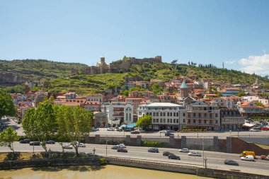 Mavi bulutlu gökyüzü ve yeşil dağların arka planında Tiflis ve nehrin güzel manzarası