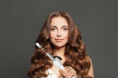 Güzel kahverengi saçlı, uzun kıvırcık saçlı, kıvırcık saçlı kadın saç maşasını gösteriyor. Saç bakımı, saç bakımı ve şekillendirme