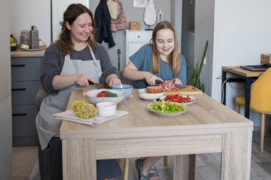 Gülen anne ve kız mutfakta eğleniyorlar. Aile bir arada. Anne kız çocuğuna yemek yapmayı öğretiyor.