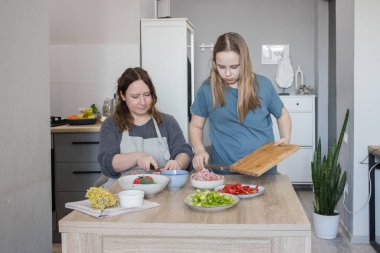 Aile bir arada. Anne kız çocuğuna yemek yapmayı öğretiyor.