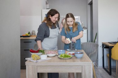 Orta yaşlı anne ve genç kız mutfakta lezzetli yemekler hazırlıyorlar. Aile bir arada. Anne kız çocuğuna yemek yapmayı öğretiyor.