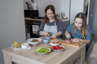 Küçük kız ve annesi birlikte ev mutfağında yemek pişiriyorlar, aile hayatı portresi yapıyorlar.